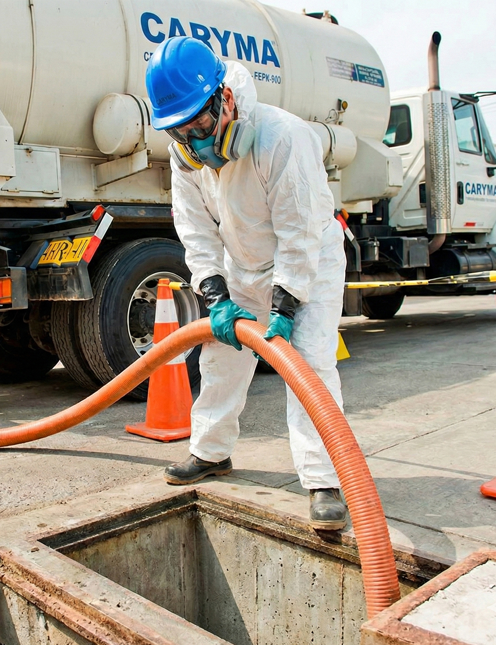 Técnico de Caryma con traje de protección y respirador realizando la succión de residuos líquidos desde una poza con manguera de alta presión.