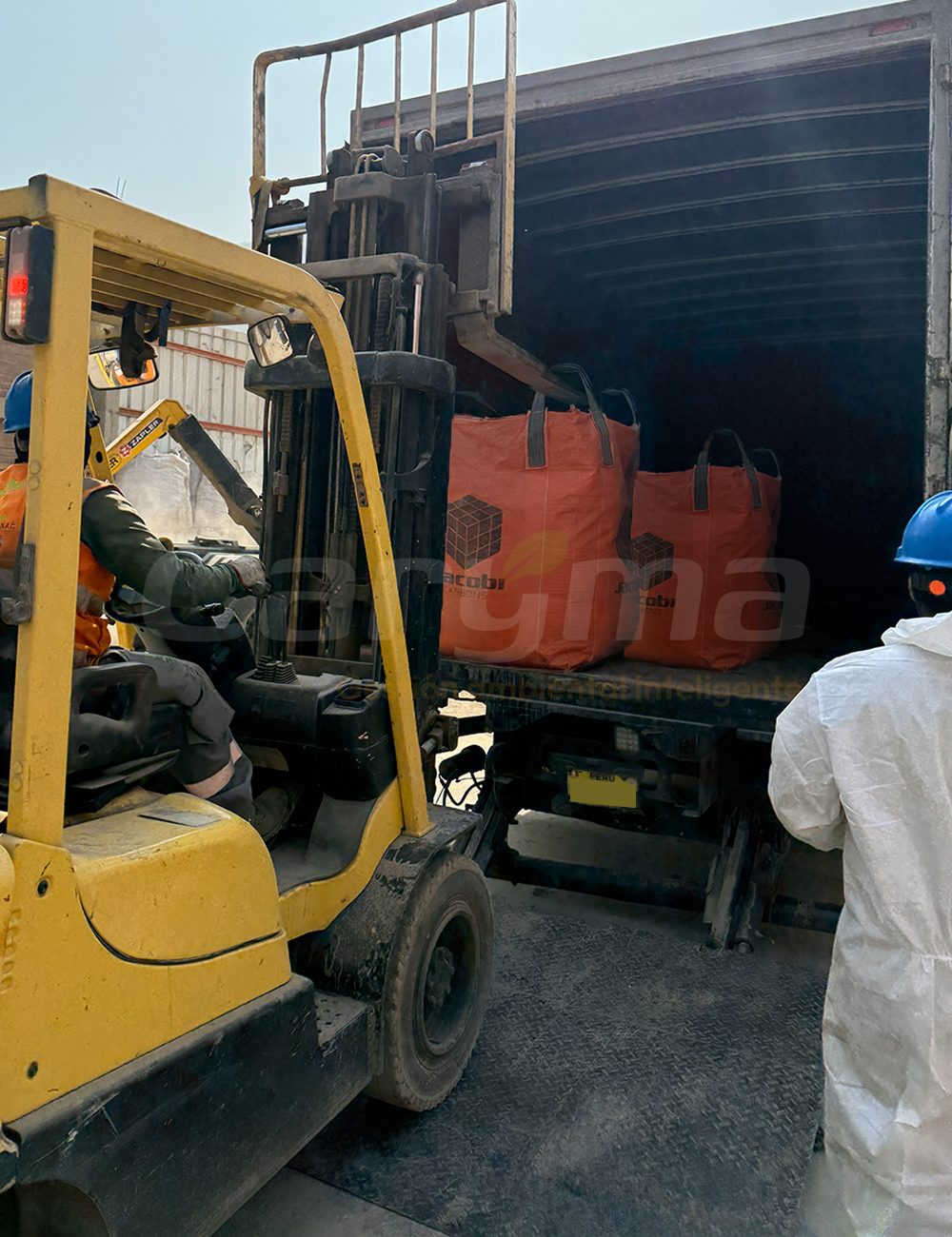 Montacargas de Caryma realizando la carga de sacos Big Bag con residuos peligrosos en un camión con furgón cerrado, bajo supervisión técnica con EPP.